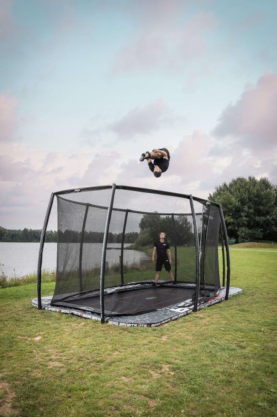 BERG Pro Bouncer FlatGround trampoline with safety net on a lawn beside a lake